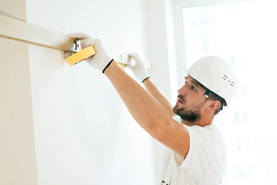 AS Home Solutions MD finisher in hard hat and gloves sanding a wall smooth