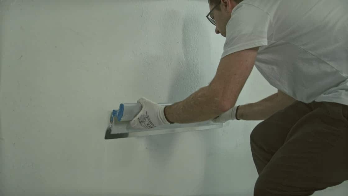 Close-up of a taping knife drawing compound across a fresh drywall joint